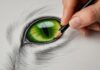 Extreme close-up, hyperrealistic photograph. A skilled hand delicately sketches the almond-shaped, vibrant green eye of a tabby cat with a sharp graphite pencil on textured paper. Intricate details of the iris, visible paper texture, and precise pencil strokes. Soft, diffused window light. Shallow depth of field, focus on the eye and pencil tip. No text, letters, or words in the image. Artefact-free, anatomically correct, perfect realism.