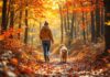 Hyperrealistic photorealistic image: A woman and a golden retriever dog are hiking on a winding forest path in peak autumn foliage. Vibrant red, orange, and yellow leaves cover the ground and trees. Sunlight filters through the dense canopy, creating dappled light and shadows. Shallow depth of field, sharp focus on the woman and dog, blurring the background forest. Warm, natural lighting. Peaceful, serene, joyful mood of companionship. No text in the image.